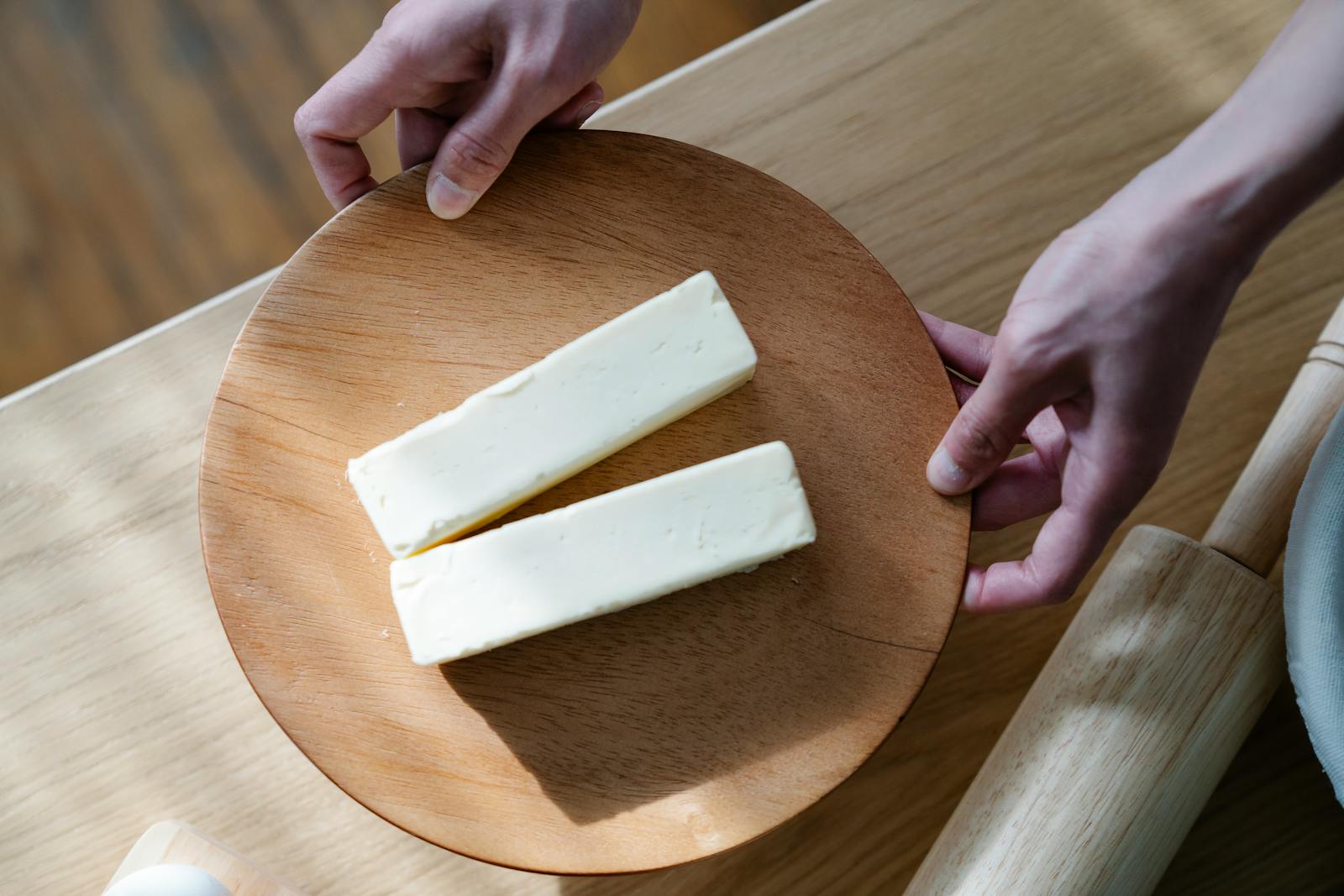 Close-up of hands holding a wooden plate with two butter sticks. Ideal for food and culinary themes.