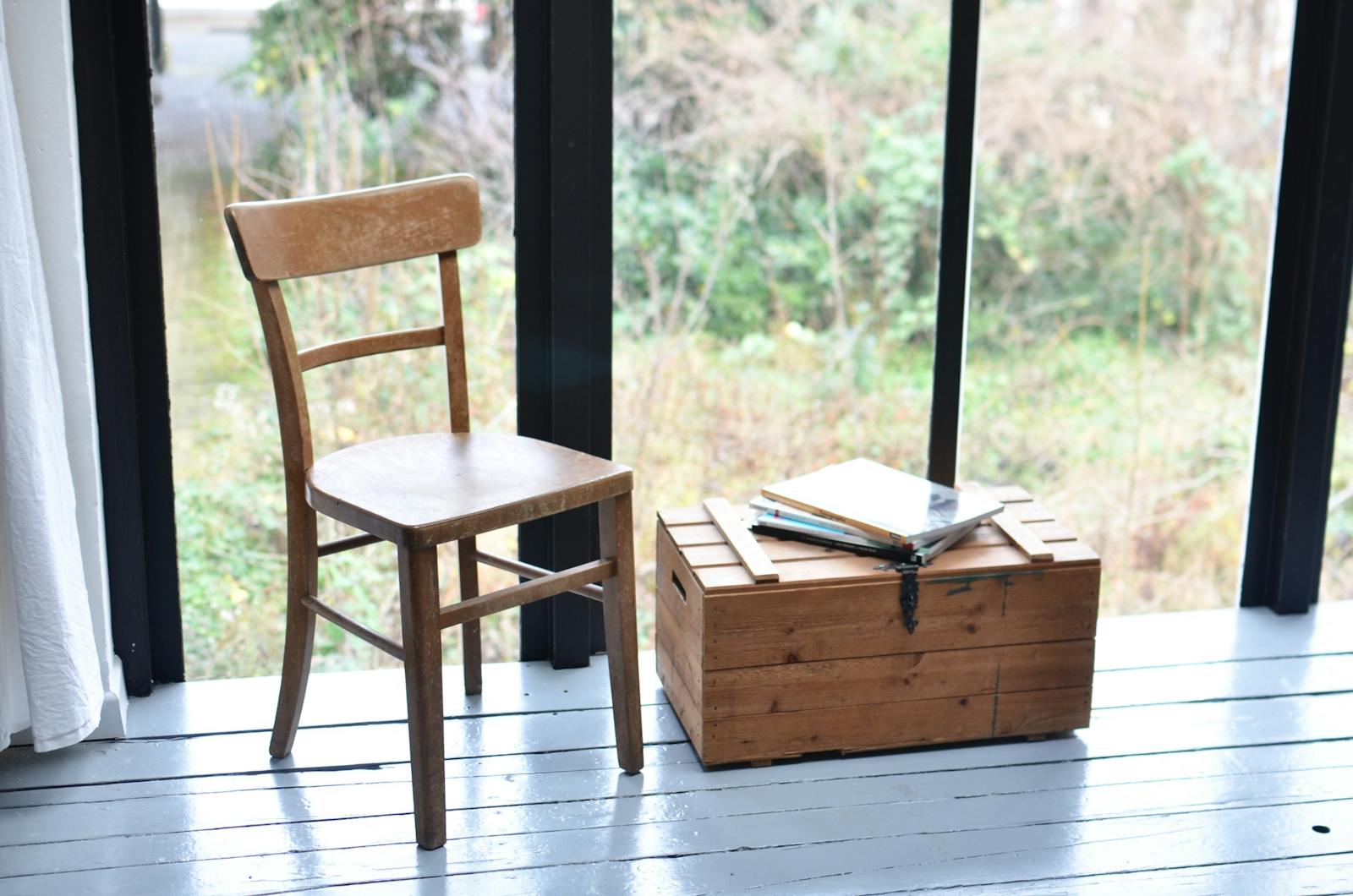 Seat made of wood and low old fashioned box with stack of books placed in front of wide window in modern room